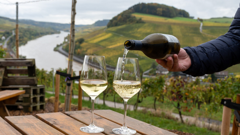 Person pouring white wine on a table with a view over looking Germany's Mosel River Valley near Trier