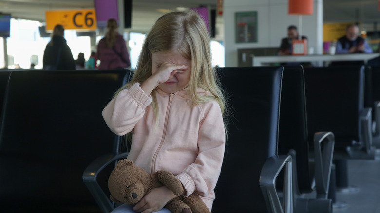 Kid crying at an airport while holding a stuffed animal bear