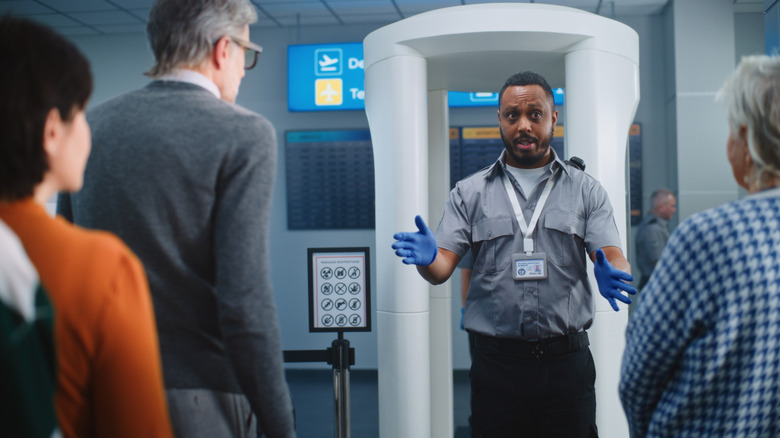 Passengers waiting to pass through a body scanner at an airport security checkpoint