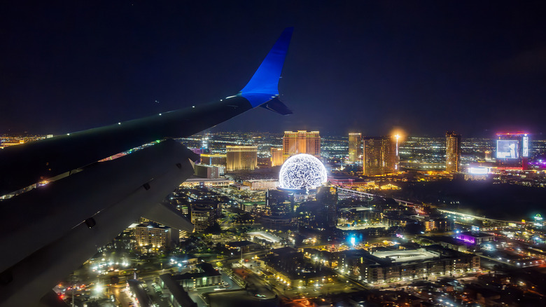 The wing of a plane over the Las Vegas Strip at night, with brightly illuminated buildings below