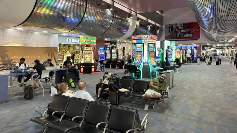 Interior of Harry Reid International Airport terminal, with passengers seated near slot machines
