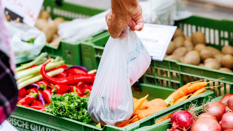 A hand grips a plastic bag over crates of produce at a market in Villach