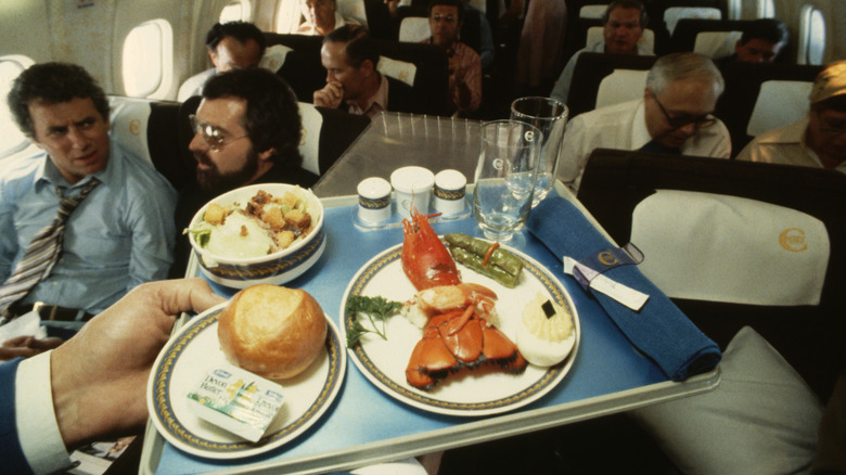 A lobster dinner is served on the Concorde, with passengers in their seats in the background.