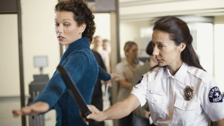 TSA agent using metal detector on a passenger with their arms wide