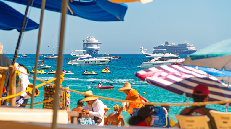 Tourists on the beach in Cabo San Lucas, Mexico with boats and cruise ships in the ocean.
