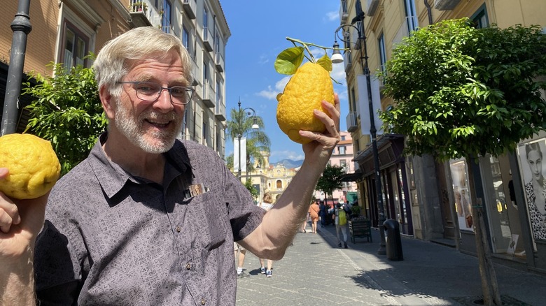 Rick Steves holds two large lemons in the middle of a street