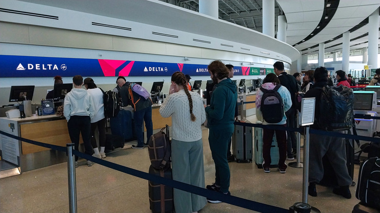 Passengers wait in line at Delta Air Line counter at an airport.