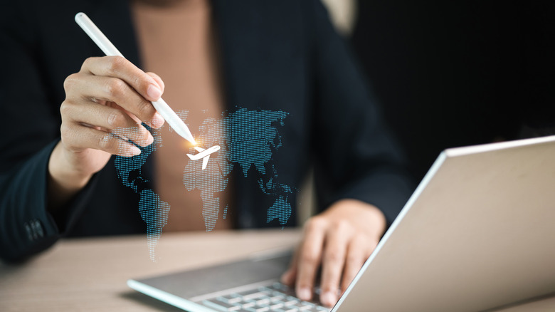 Person using a stylus to move a white plan around the a holographic globe in front of a silver laptop