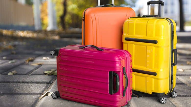 Three colorful suitcases outside on paved sidewalk.