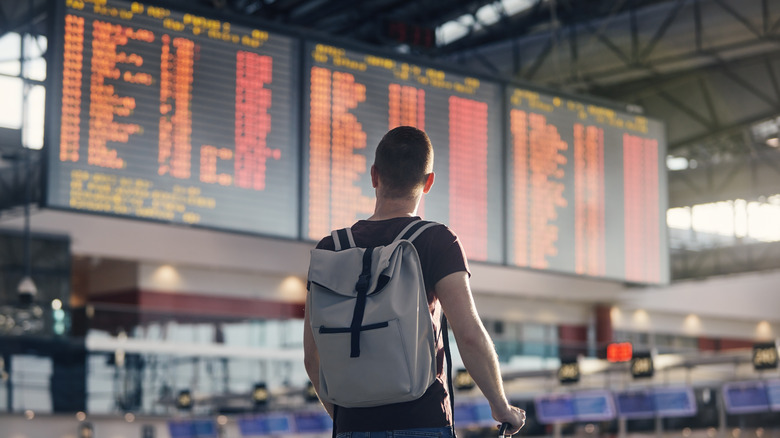 A man wearing a backpack checks the flight info board at an airport in Germany.