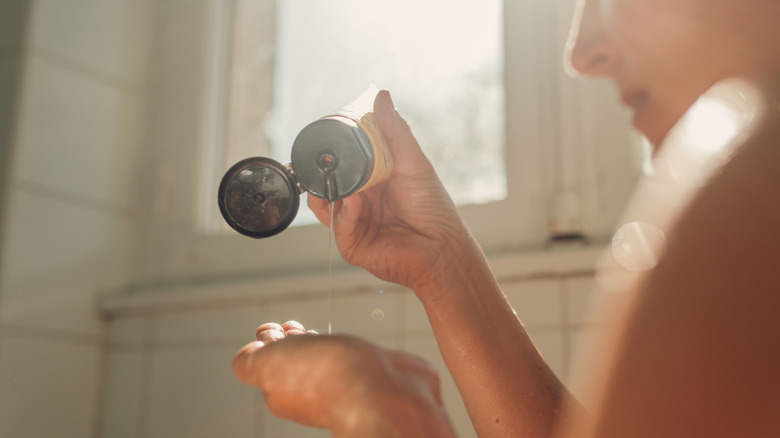 A woman putting shampoo into her hand while in a shower