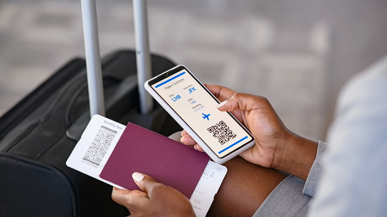 Someone holding a phone displaying flight information, with a boarding pass and passport in their other hand