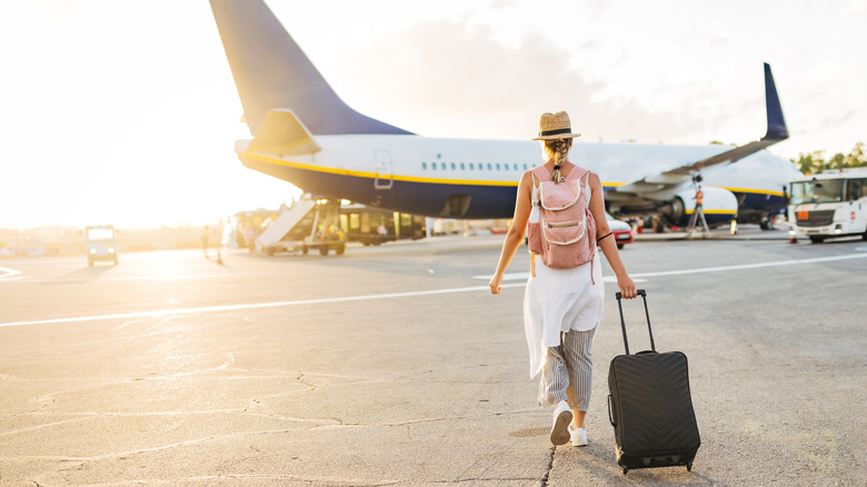 Someone with a rolling suitcase walking to a plane at an airport