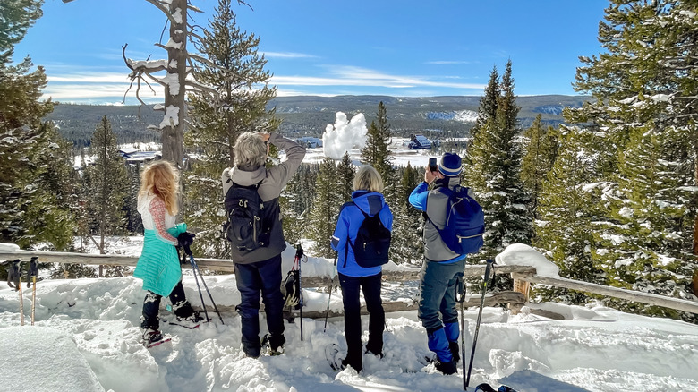A family watching Old Faithful erupt in Yellowstone National Park, surrounded by snow