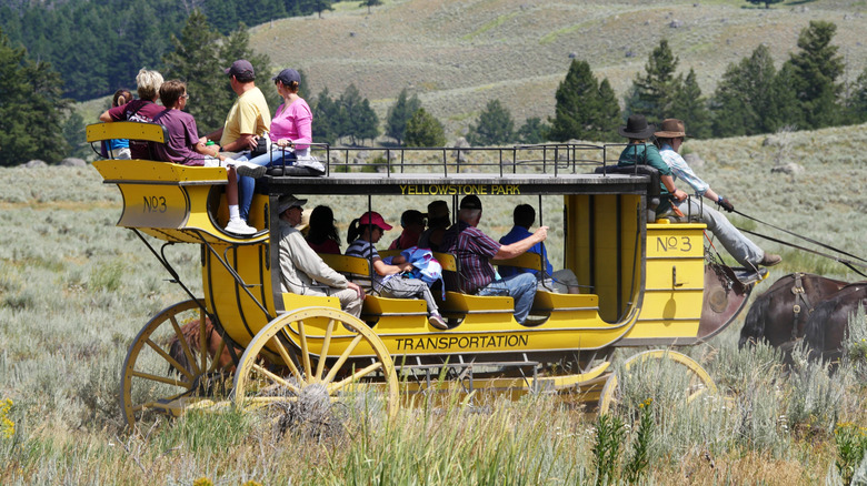 People on a yellow stagecoach riding through Pleasant Valley, Yellowstone National Park