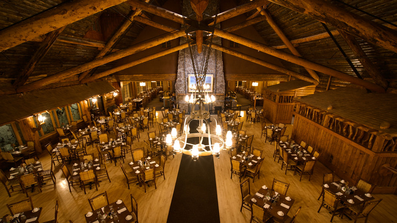 High view of restaurant dining tables, wooden ceiling beams, and a chandelier in a cabin dining room