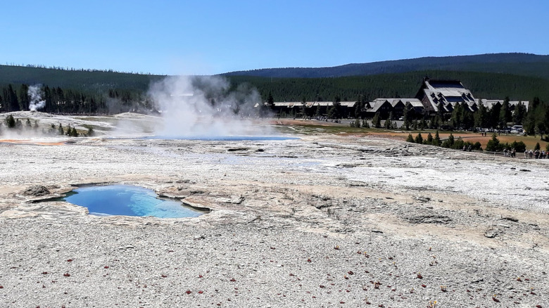 Grey ground with steaming blue pools, a lodge, and a blue sky in the background