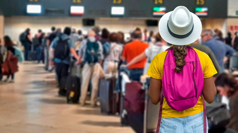 A woman stands in a long line at the airport, wearing a pink backpack.