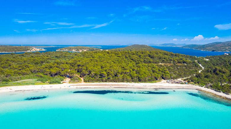 Wide angle view of Sakarun Beach shoreline, turquoise water and forests in background.