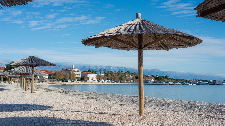 lines of beach umbrellas by the water with mountains in the distance