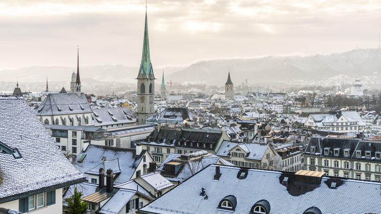 Cityscape of Zurich with mountains in the background during winter, with snow-topped roofs among the towers