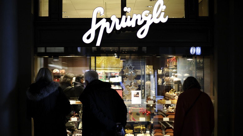 Three people back lit against the window of Sprüngli chocolatier in Zurich at night