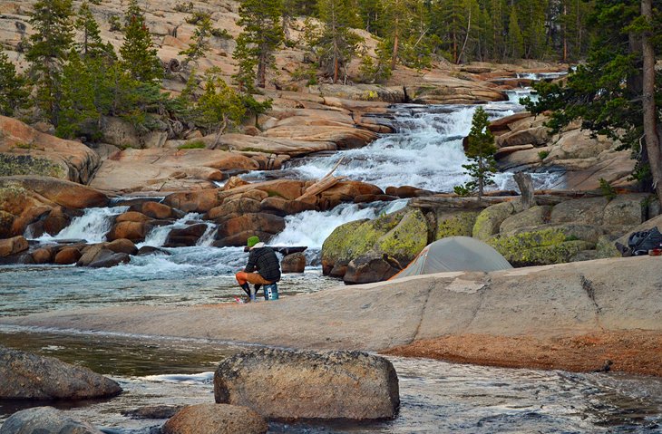 A thru-hiker makes dinner on the banks of Tuolumne Falls