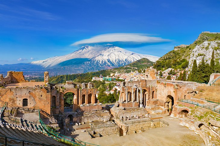 Ancient Greek theater ruins in Sicily with snow-covered Etna Volcano in the distance