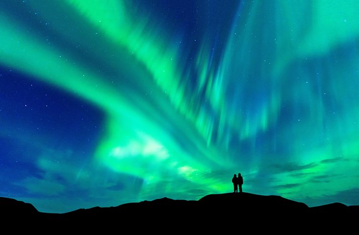 Couple enjoying the colorful aurora borealis in Iceland