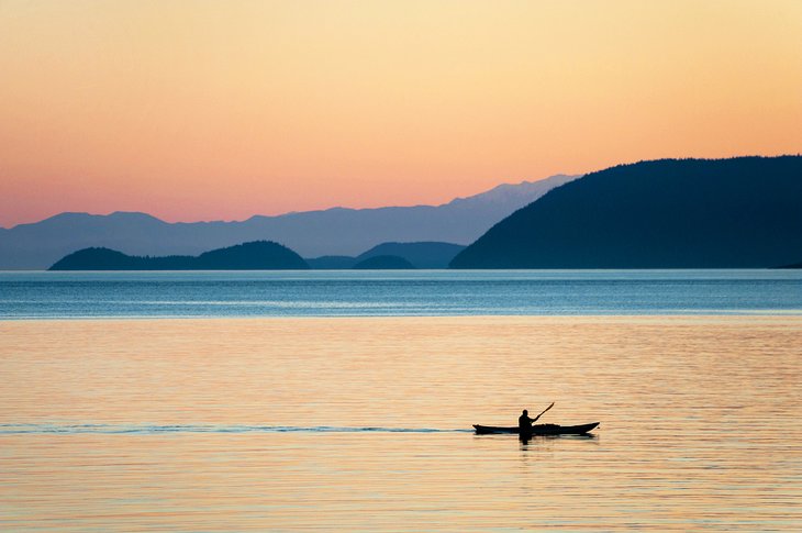 Kayaker paddling past Orcas Island at sunset